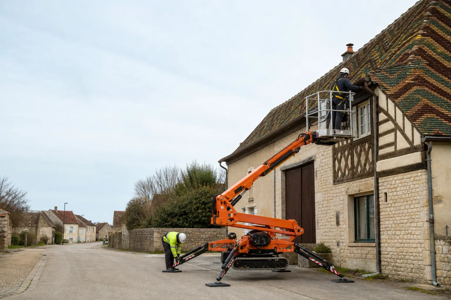 Une nacelle araignée élève un couvreur près de toits bourguignons en tuiles vernissées.