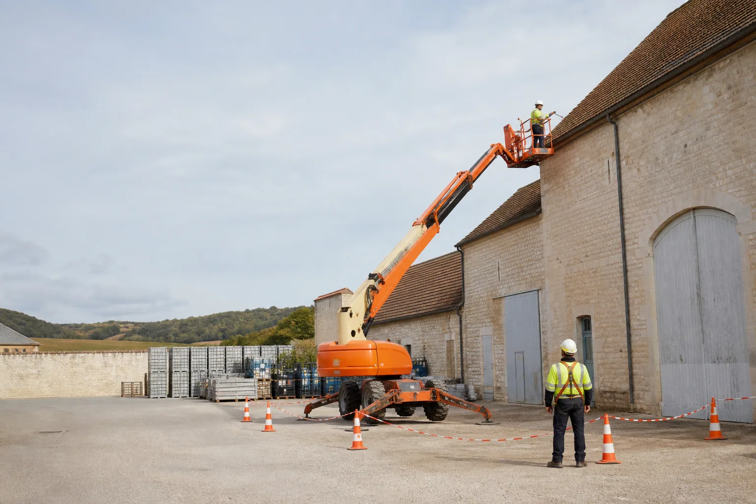 Une nacelle élévatrice orange intervient sur un bâtiment avec un technicien dans le panier et un opérateur au sol, dans le secteur de Beaune.
