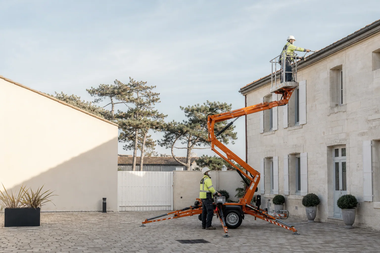 Une nacelle élévatrice orange intervient sur un bâtiment avec un technicien dans le panier et un opérateur au sol, dans le secteur de La Rochelle.