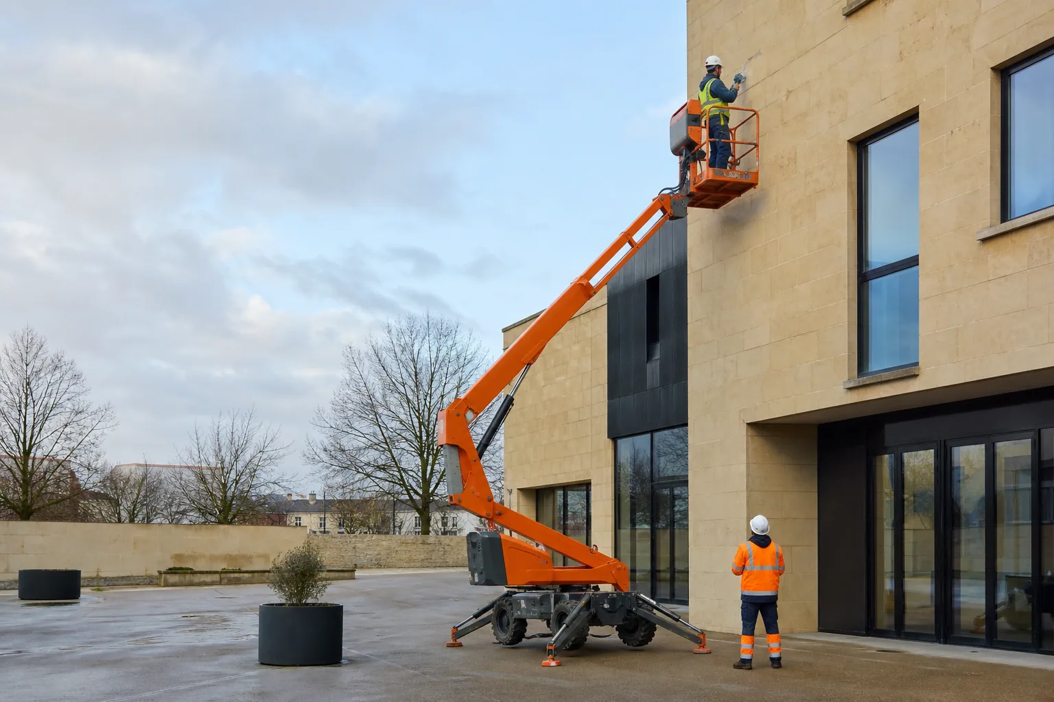 Une nacelle élévatrice orange intervient sur un bâtiment avec un technicien dans le panier et un opérateur au sol, dans le secteur de Metz.