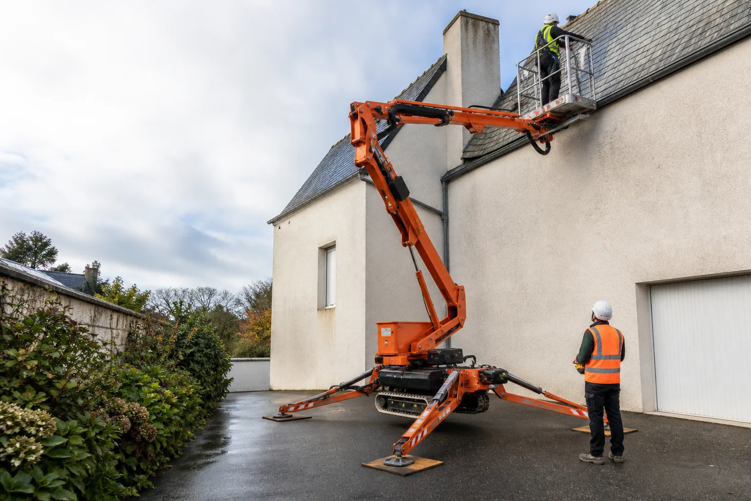 Une nacelle élévatrice orange intervient sur un bâtiment avec un technicien dans le panier et un opérateur au sol, dans le secteur de Saint-Lô.